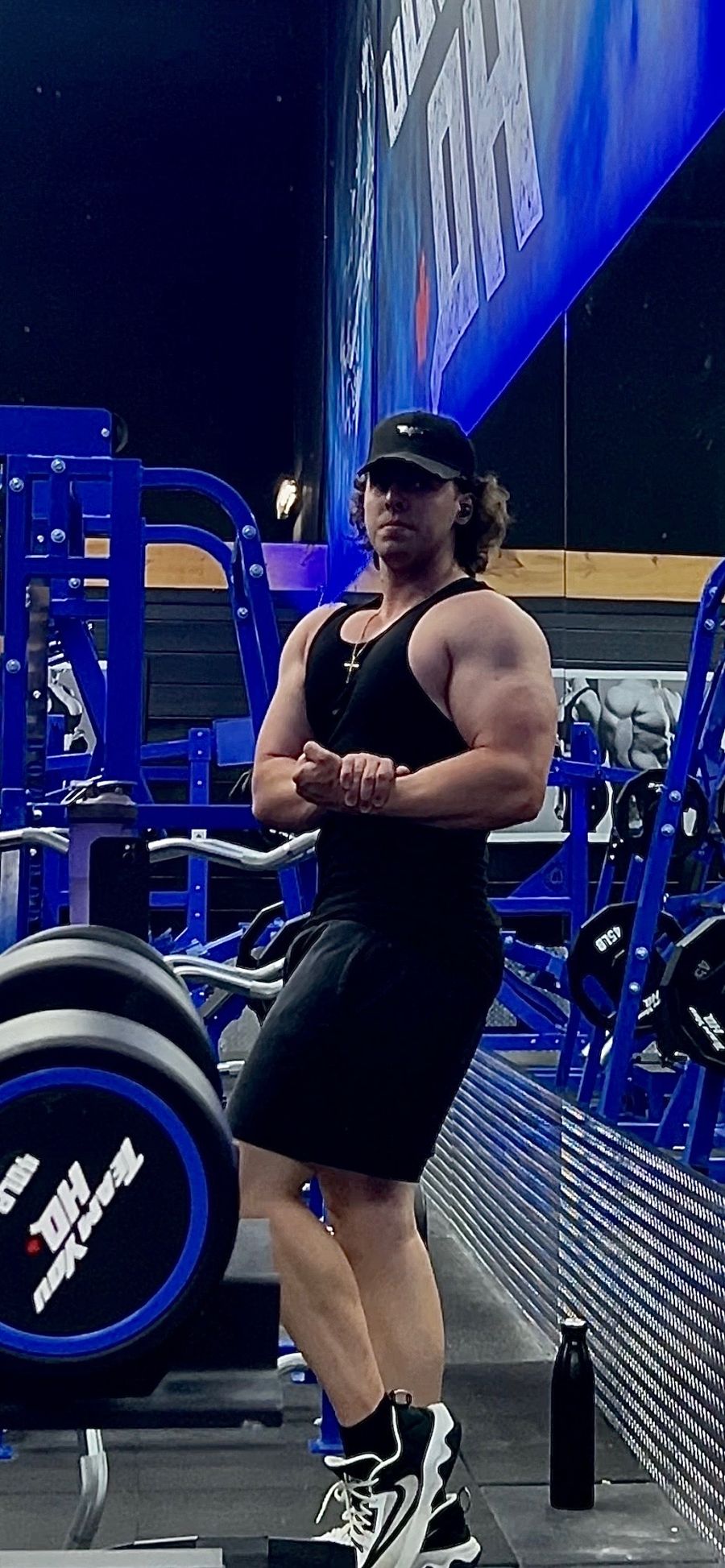 Sam in a black tank top at the gym, arms crossed in a flex